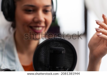 Closeup of woman influencer talking into microphone. Podcast presenter with headphones using recording equipment for live broadcast. Audio streaming for internet online radio production.