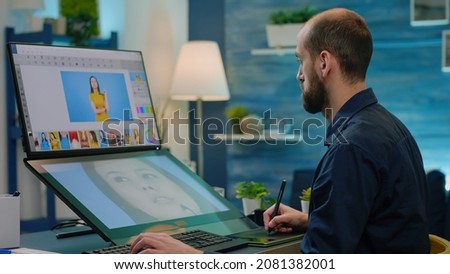 Photography artist editing photos with graphic tablet and stylus while using touch screen monitor with retouching app. Man photographer doing retouch work on pictures for media project.