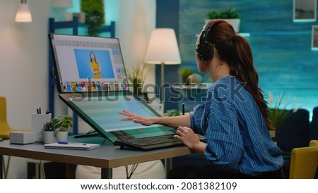 Woman photographer wearing headphones and editing pictures with retouching app on touch screen monitor. Photography editor doing retouch work using device and graphic tablet with stylus