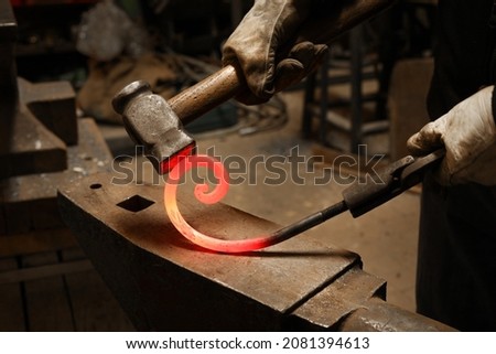 Close up view of heated metal and anvil. The blacksmith in the production process of metal products handmade in the forge. Blacksmith forging metal with a hammer. Royalty-Free Stock Photo #2081394613