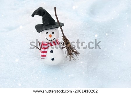 winter nature background. cute Snowman toy in witch hat with broom on snow. Christmas, New Year holidays. festive winter season. cold snowy weather. copy space