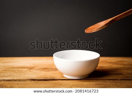 A white ceramic cup, a wooden spoon above it on a wooden table.
