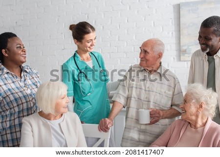 Positive multiethnic patients standing near young nurse in nursing home