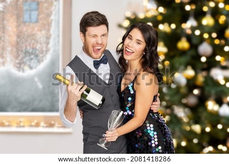 celebration and winter holidays concept - happy couple with bottle of non alcoholic champagne and wine glasses at party over christmas tree lights background
