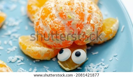 Fruit turtles, a snack made of fresh parts of mandarins served in the shape of water turtles on a blue plate, funny food