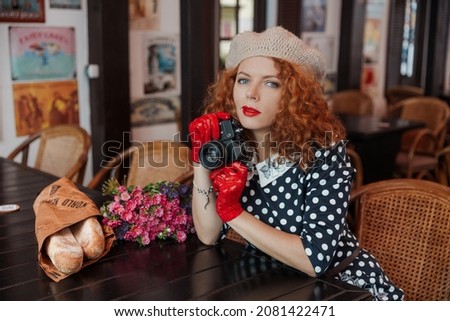 A woman in a beret and vintage dress holds a camera in her hands and takes shoots