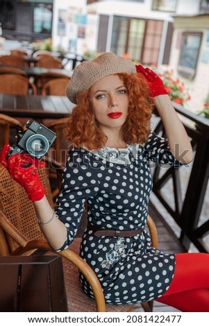 A woman in a beret and vintage dress holds a camera in her hands and takes shoots