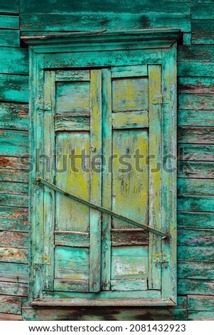 A window with closed shutters of an old wooden house, with a peeling green color, a fragment of the facade. The picture was taken in Russia, in the city of Orenburg