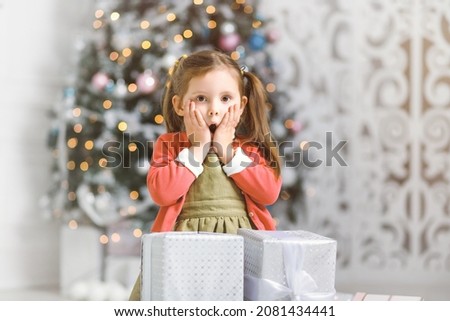 Emotional girl surprised by the abundance of New Year gifts by a Christmas tree in cozy room.