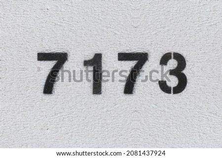 Black Number 7173 on the white wall. Spray paint. Number seven thousand one hundred and seventy three.