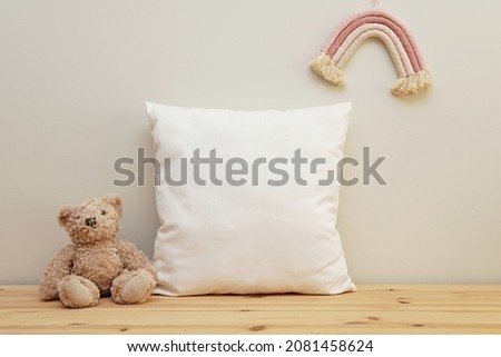 White cotton square baby girl pillow mockup for design presentation, minimal composition on wooden shelf with toy bear and boho rainbow wall decoration. Royalty-Free Stock Photo #2081458624