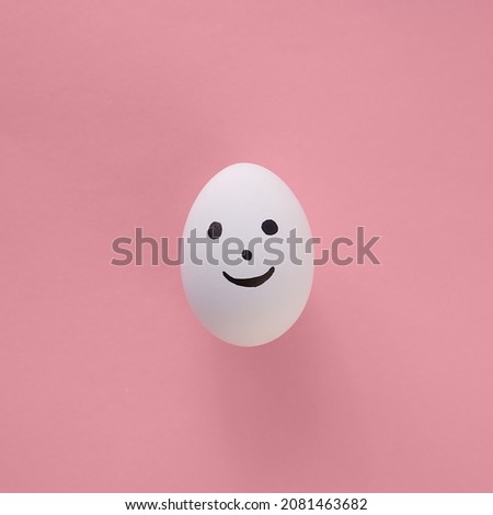 
One emoji egg with a smile on its face is set against a light red and pink paper background. Copy space. 