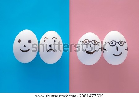 Family concept no people. Two couples with different emotions. One pair of eggs in glasses on a pink background, holding hands and smiling. The second couple is on a blue background, separated and sad