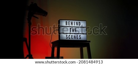 Behind the scenes text on Lightbox or Cinema Light box. Movie board light box on studio stair and light Snoot tripod on colors gradiant Background. Represent behind the scenes team is working on.