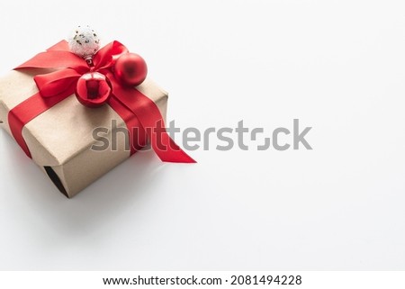 A Christmas gift in craft packaging with a red ribbon and Christmas balls. Festive card with place for text. Horizontal photo.