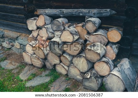Close up of stacked firewood in front of a wooden hut. Picture with matte effect