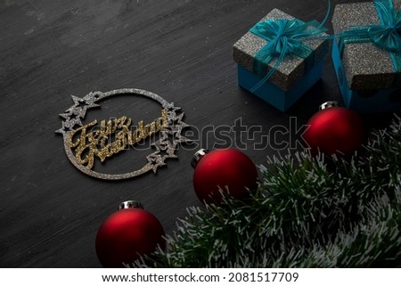 golden merry christmas sign on a black background with red spheres and gifts with blue bow.