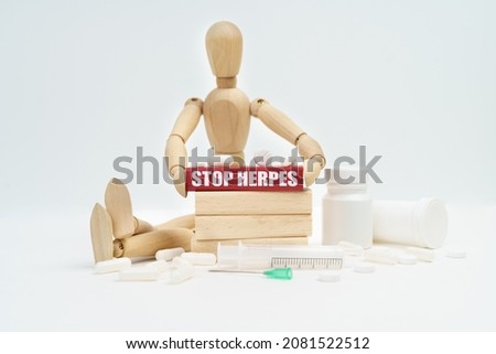 Medicine and healthcare concept. A figurine of a man sitting among pills lifts a red wooden block with an inscription STOP HERPES from a wall of blocks.