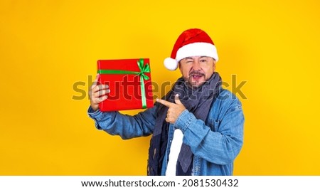 latin senior man holding Christmas presents with santa hat on yellow background in Mexico Latin America
