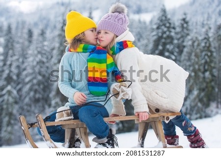 Kids kiss lovely. Kids boy and little girl enjoying a sleigh ride. Children kissing together, play outdoors in snow on mountains in winter. Kids Christmas vacation.