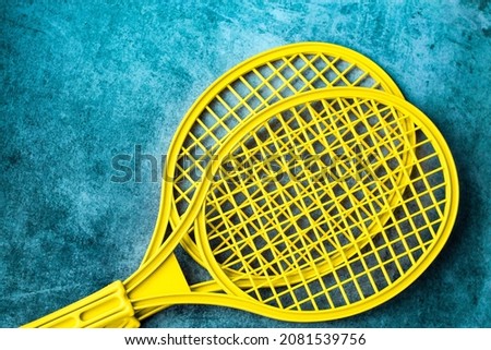 two plastic tennis rackets of bright yellow color on a worn turquoise background; a children's version of the badminton tournament
