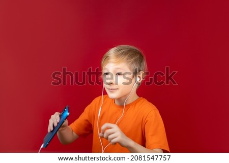 funny boy holding a blue phone in his hands, to which white headphones are connected, he is listening to music