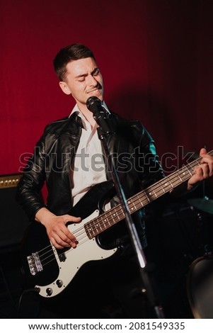 Talented handsome young guitarist man singing a song in studio recording on red background surrounded by instruments. Passion, hobby, singer, electric guitar Royalty-Free Stock Photo #2081549335