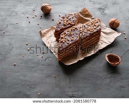 Homemade chocolate honey cake slices with cream and walnuts on kraft paper on a dark background with space for text. Top view Royalty-Free Stock Photo #2081580778