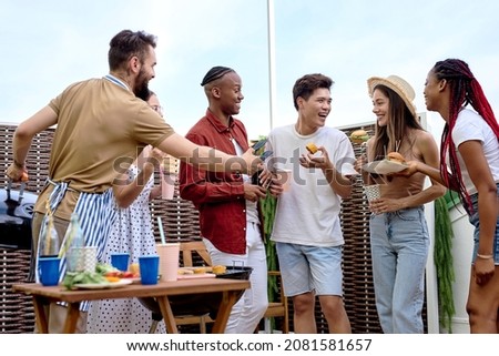 Young positive men and women having barbecue party on the evening on house patio. people doing bbq dinner outdoor cooking meat and drinking lemonade, eating burgers. Food, fun and friendship concept