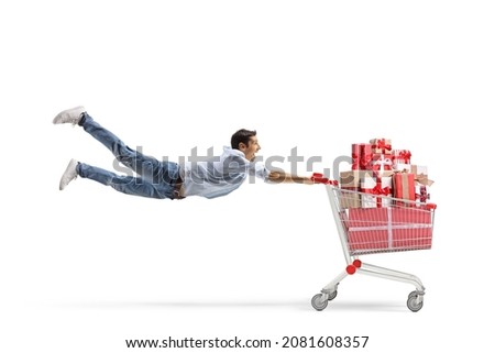 Full length shot of a casual young man flying with a shopping cart full of presents isolated on white background