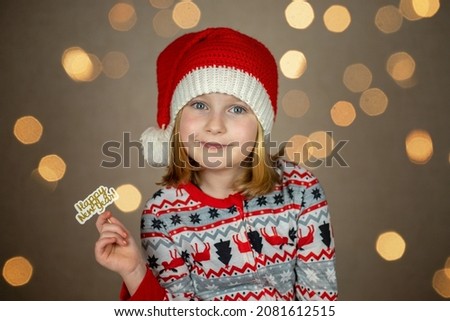 a girl in a santa hat holds a happy new year sign on a new year bokeh background.