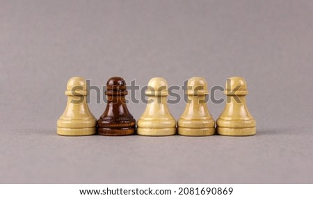 One black chess pawn among whites pawns on gray background Royalty-Free Stock Photo #2081690869