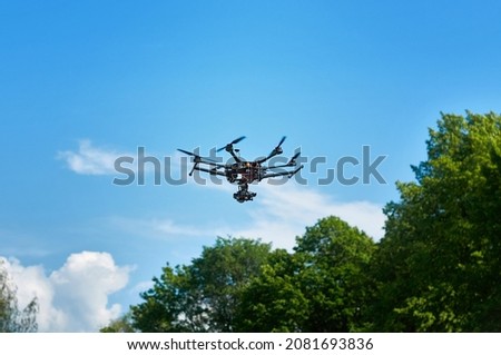 Drone with camera flying in the blue sky above the trees. Shooting photos and video from the air. Quadcopter in the forest.