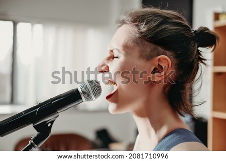 young emotional woman singing into a microphone. female rock singer on a rehearsal in record studio. side view.