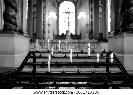 Black and white picture of lighted candles in front of an altar inside a church with stained glass window and cross in blurry background