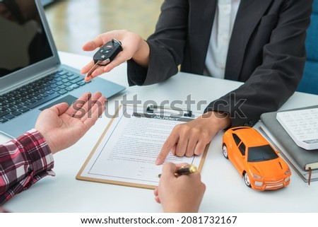 Sale agent handed over the rental car key to the customer who signed the contract and the terms of the agreement on the document, Car rental service and Insurance car concept.