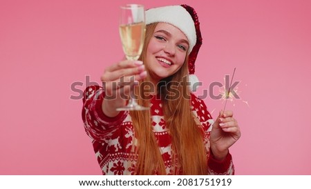 Joyful Christmas Santa adult cute girl dancing with bengal sparklers fireworks and champagne glass, sending wishes and congratulation on red background. Happy New Year celebration merry holiday