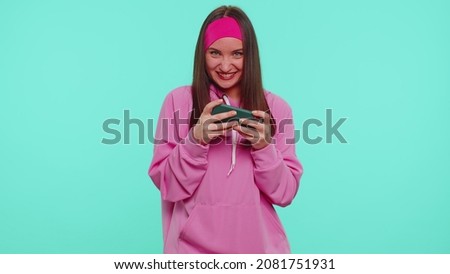 Worried funny addicted woman enthusiastically playing racing video games on mobile phone. Young adult teen girl using smartphone gadget app with drive simulator isolayed on blue studio wall background