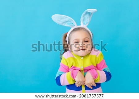 portrait of a little girl with rabbit ears in a striped jacket. The concept of the Easter holiday. Blue background, photo studio, place for text