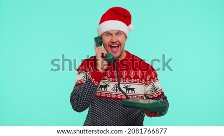 Hey you, call me back. Lovely man in red New Year sweater talking on wired vintage telephone of 80s, says hey you call me back on blue studio wall background. Happy Christmas celebration merry holiday