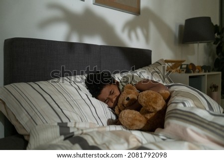 Scared African American boy embracing bear toy while sleeping in bed and having nightmares Royalty-Free Stock Photo #2081792098