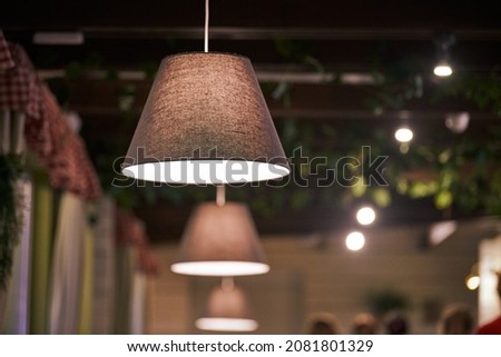 Pendant lamps over tables in city cafe, evening lighting restaurant. Beige fabric lampshades with low dimmed warm light. Modern cozy interior, country style pendant lighting Royalty-Free Stock Photo #2081801329
