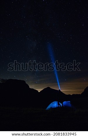 Picture of the nightsky with a person with a flashlight and a tent in the foreground.