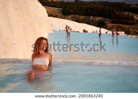 Pamukkale travertine in Turkey with woman enjoying the views. Red hair woman traveler swimming at Pamukkale Natural Park and looking at beautiful sunset.Sexy young woman rest in Pamukkale.        Royalty-Free Stock Photo #2081863240