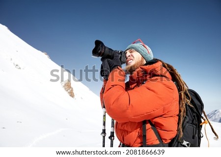 Photographer with camera taking a picture in red jacket at the snow mountains against blue sky in Almaty, Kazakhstan 