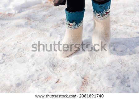 White felt boots with ornament. Close-up of man feet shod in felt boots and standing on fresh snow that fell after heavy snowfall.