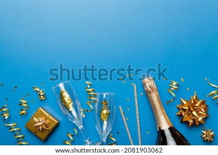 Bottle of champagne with colored glitter, confetti and gift box space for text on colorfull background, top view. Hilarious, christmas and birthday celebration.