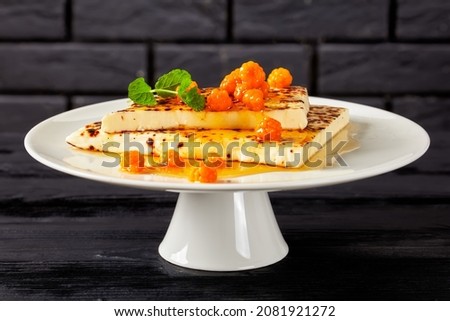 Leipajuusto, kaffeost, bread cheese, finnish squeaky cheese slices with cloudberry jam and fresh mint on a white cake stand with black brick wall at the background Royalty-Free Stock Photo #2081921272