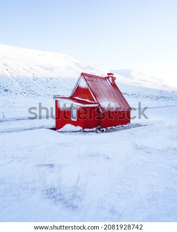 Alone snow covered house in Iceland mountains. Lonely abandoned red wooden house at the foot of snow-covered mountain in Iceland. Winter northern scenery. High quality photo
