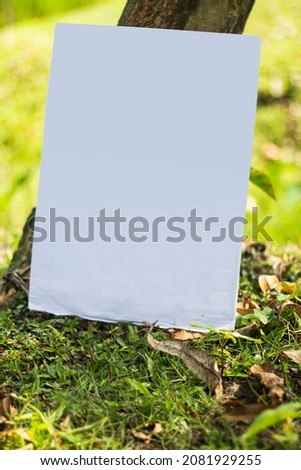 A white signboard leaning against a tree on the ground and the background behind it is blurred green.
